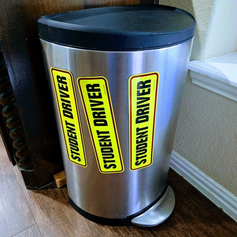 Trash can with three "student driver" magnet stickers attached.