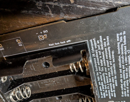 The backside of the Eurofurence Cyberbadge Supersponsor gift showing a silkscreen text "Nazi furs fuck off!"