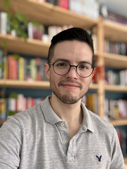 Selfie wearing a grey polo shirt, in front of my bookcase.