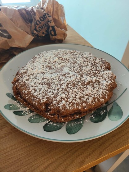 Photo de la frucandie entière (le gâteau est rond et couvert de sucre glace) posée sur une assiette blanche à motif feuille d'eucalyptus. L'assiette est elle-même posée sur un plan de travail en bois blond.