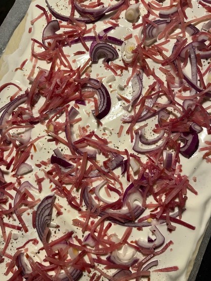 Flammkuchen mit Zwiebeln und Speck vor dem backen.