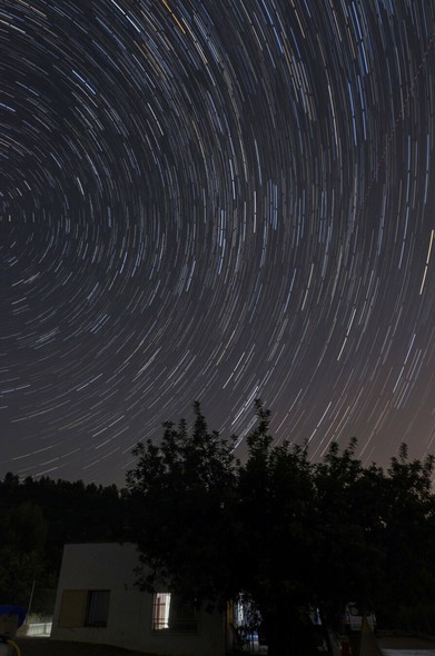 Night photo, circumpolar star trails above a house and a centenarian tree in the countryside, near Valencia.
