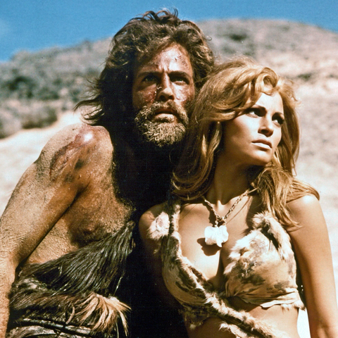 Raquel Welch in a scene from “One Million Years BC”, standing next to a bearded, rather rough looking Stone Age man (Tumak, played by John Richardson) and wearing a furry bikini… as women did in those days.