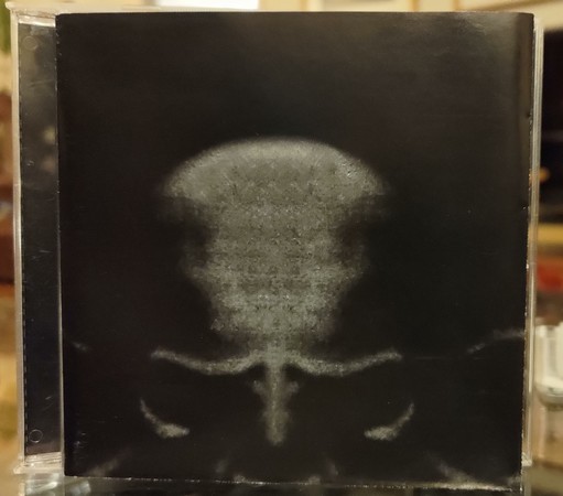 CD booklet before jewel case cover. Mostly black, with a dark, grey skull-like form. No text.