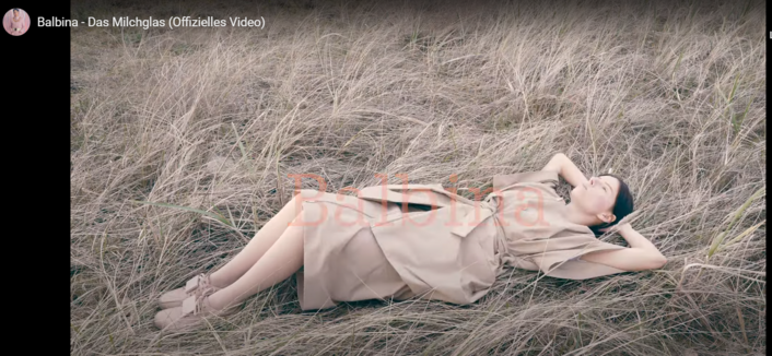 Screenshot 26.02.2025 Balbina im "Gras" liegend, die Hände hinter dem Kopf verschränkt und in den Himmel guckend. Szene aus dem Musikvideo "Das Milchglas" - genau meine Symbolik :-) :-) :-)