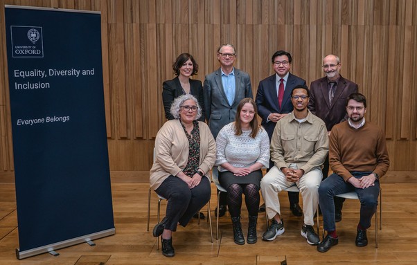 A group photo from the University of Oxford’s EDI Roundtable on Neurodiversity, featuring speakers and organisers. Seated in the front row are Professor Kate Watkins, Antonia Johnson, Jonathan Brooks and Dr Dionysios Kyropoulos. Standing in the back row are Professor Liz Pellicano, Professor Jonathan Wolff, Professor Tim Soutphommasane and Dr Laurence Leaver. To the left, an EDI banner reads: "Equality, Diversity and Inclusion – Everyone Belongs". The setting is a conference room with wooden paneling.