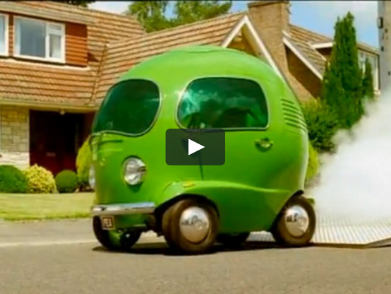 A scene of a green cartoon style car speeding on a suburban lane. The car is almost poerfectly spherical, bright green, and looks a bit like a volkswagen transporter from the 60's. A white cloud of smoke comes out of the back of the car, making it look like it's speeding.