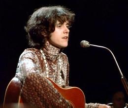 Donovan, con una blusa hippy y una guitarra rojiza, actuando sobre el escenario en 1966. Es un chaval joven de fuerte mandíbula y mirada algo triste. Lleva el pelo medio largo y algo despeinado. Discogs.