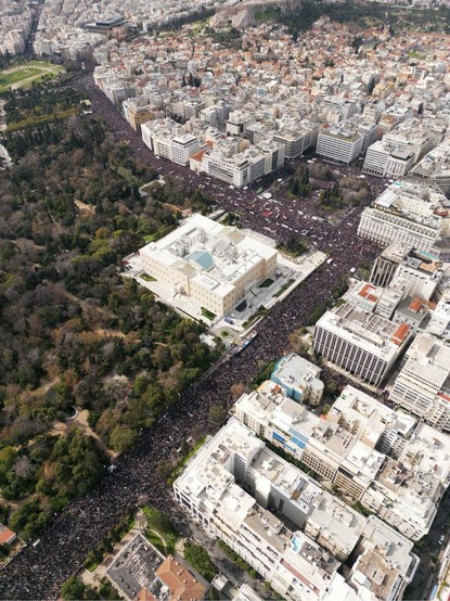 A sea of people demonstrating in Athens, Greece. The Parliament is at the center of the image, and the hill of Acropolis can be seen at the upper edge.