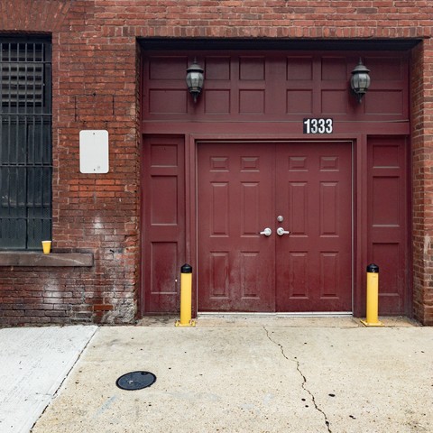 A yellow plastic cup on the windowsill of outside a building next to a garage door with two yellow barricades