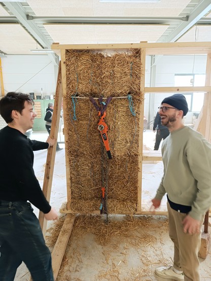 2 carpenters having fun learning straw building. Straw vale timber module with chain hoists  to add pressure in the background.