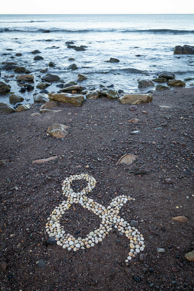 An ampersand on a beach, created by arranging some unoccupied limpet shells.