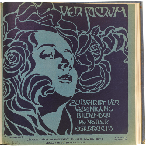 Photo of a page from a book showing the cover of a periodical. The cover features a woman with flowing hair printed in dark blue ona green paper background. Next to her is the title “Ver Sacrum [The Spring]” in organic lettering with similar flowing shapes as the illustration. At the bottom is more lettering: “ZEITSCHRIFT DER VEREINIGUNG BILDENDER KÜNSTLER / OSTERREIHES” [Magazine of the Association of Visual Artists / Easter]”