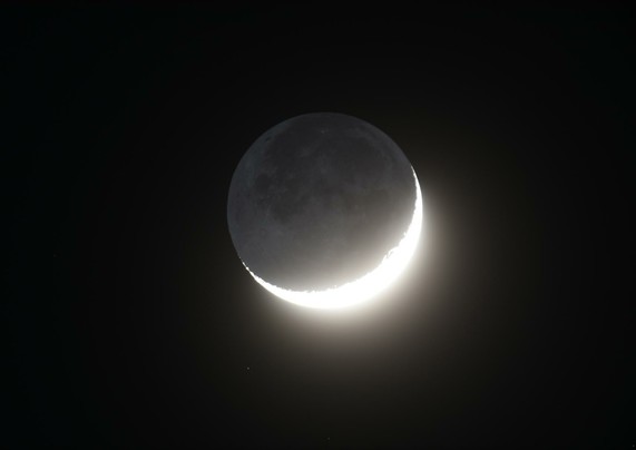 Die überbelichtete zunehmende Mondsichel am dunklen Nachthimmel, die dunkle Seite des Mondes wird als aschfahles Mondlicht sichtbar