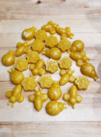 A bunch of bee, ladybug, and flower-shaped rendered beeswax in a group.