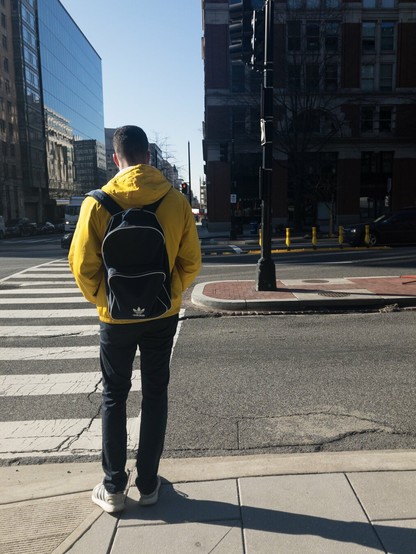 Man in a yellow jacket with a black backpack standing on a street corner