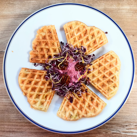 Das fertige Gericht auf dem Teller. 
5 Segmente einer runden Waffel, in der Mitte die rosa Creme mit 3 Pekanüssen und violetten Sprossen und einigen Zitronenzesten.