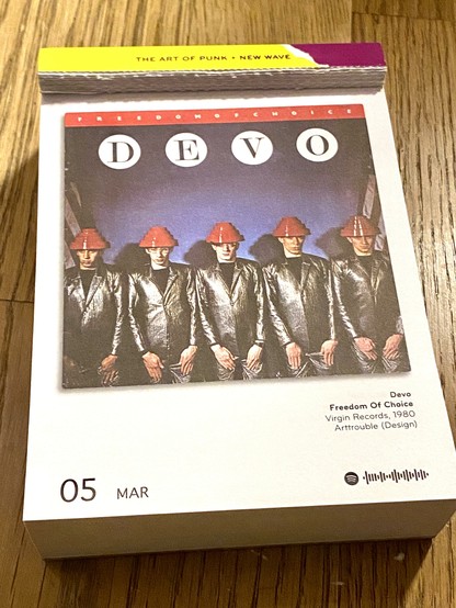 Das Bild zeigt das Albumcover von “Freedom of Choice” der Band DEVO, das 1980 veröffentlicht wurde.

Darauf sind die fünf Bandmitglieder in einer Reihe zu sehen. Sie tragen metallisch glänzende, silberne Anzüge und die ikonischen “Energy Domes”, rote, stufenförmige Hüte, die ein Markenzeichen der Band sind. Der Hintergrund ist dunkel mit einem blauen Farbverlauf, und über den Köpfen der Band steht groß “DEVO” in weißen Buchstaben, eingerahmt von einzelnen weißen Kreisen. Am oberen Rand befindet sich ein roter Streifen mit der Aufschrift “FREEDOM OF CHOICE” in kleinen weißen Buchstaben.

Das Bild ist ein bekanntes Beispiel für DEVOs stilisierte Ästhetik, die oft futuristische und satirische Elemente kombiniert.