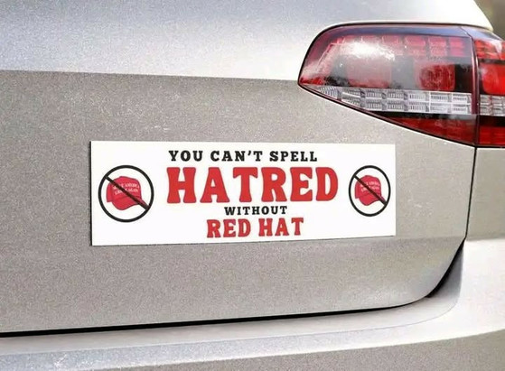 Bumper sticker on the back of a car. The sticker reads: "YOU CAN'T SPELL HATRED WITHOUT RED HAT." The words "HATRED" and "RED HAT" are in bold red letters. There are two symbols on either side of the text, each showing a red hat with a diagonal line through it, indicating a prohibition.