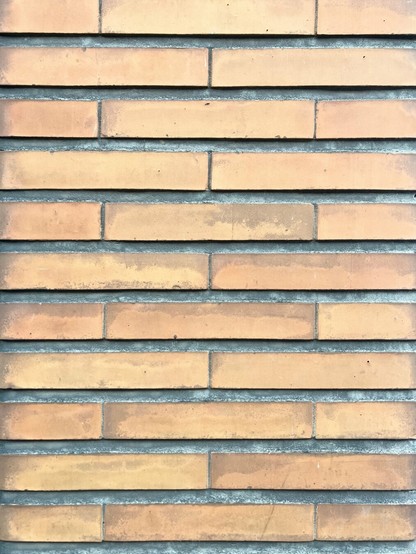 Een muur van fijne okergele bakstenen met grijze voeg