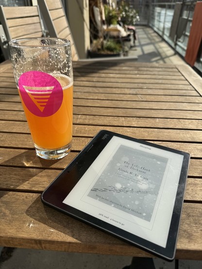 The same beer glass is now half empty sitting on a table outside in the sun next to an ebook reader.