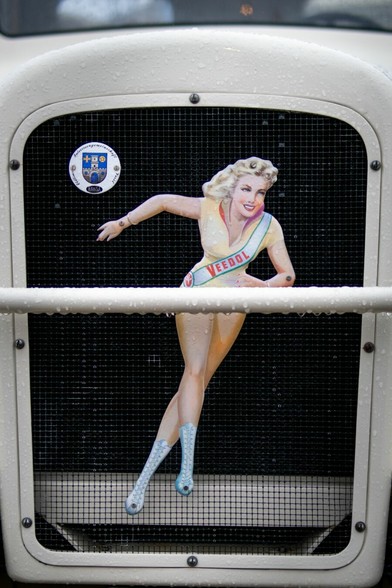 Ein Foto einer Oldtimer Motorhaube. Auf der Motorhaube ist ein Pin-Up Girl zu sehen. Sie trägt eine Schärpe auf der Veedol steht.