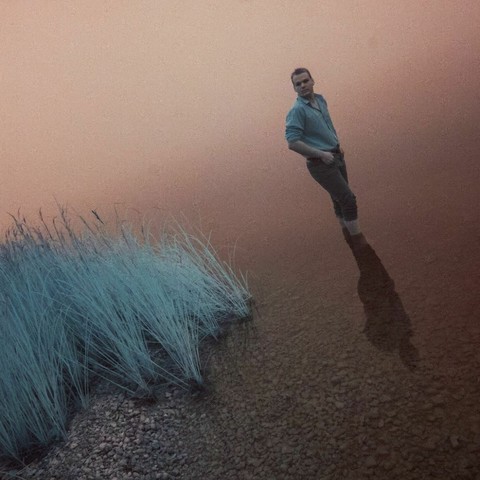 John les pied dans l'eau rouge avec quelque herbe bleu au tour de lui.