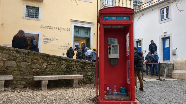Uma cabine telefónica vermelha. Algumas pessoas em plano de fundo.