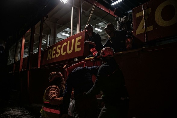 Menschen steigen in dunkler Nacht von einem RHIB auf die SEA EYE 4. Licht kommt nur von der Decksbeleuchtung des Schiffs.