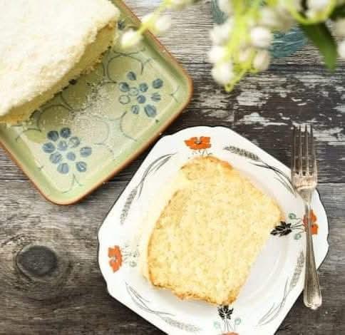 A soft and fluffy coconut cake on a platter and a slice of a tea plate.