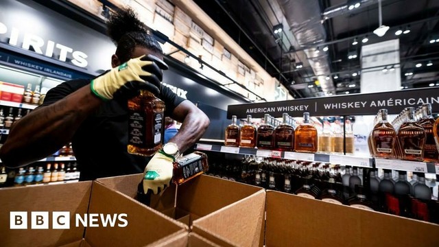 A man filling Jack Daniel's bottles in a shipping box. The background has shelves full of Jack Daniel's bottles