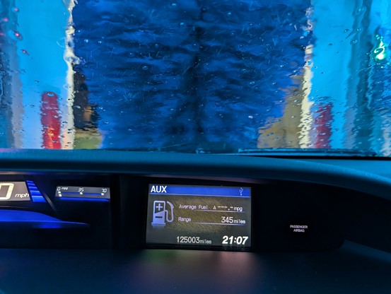 In an automatic car wash. Lights are all blue with a blue brush scrubbing the front. Odometer reads 125,003 miles. Tank is full.