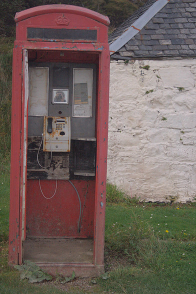 An old red public telephone box on the island of Canna, one of the small isles off the West coast of Scotland. The door of the telephone box is missing and it looks rather weather beaten and neglected.