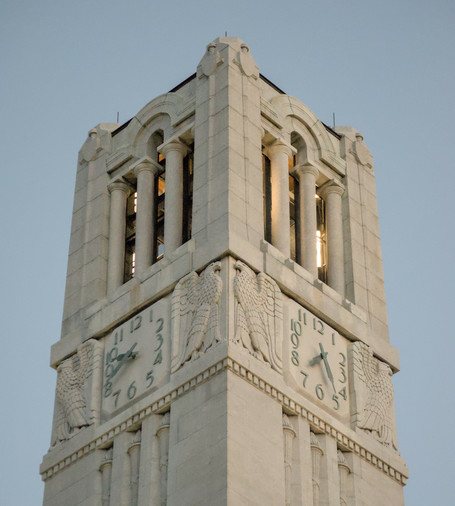 A close up photo of the top of the belltower, showing the clocks and eagle reliefs that decorate it.