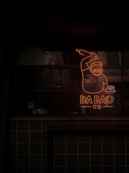A dimly lit image of the façade of Da Bao Restobar with the neon sign lit and reflections of the street across reflecting on its windows.