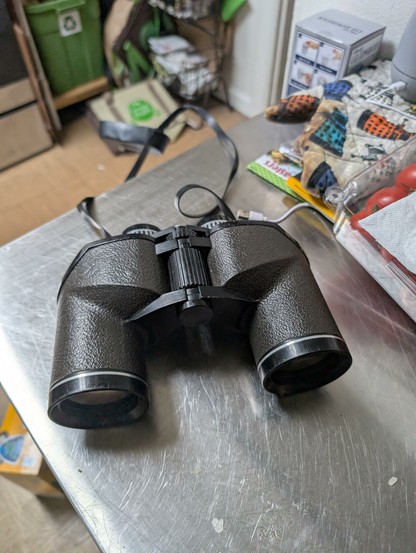 Battered black binoculars sitting on a metal countertop.
