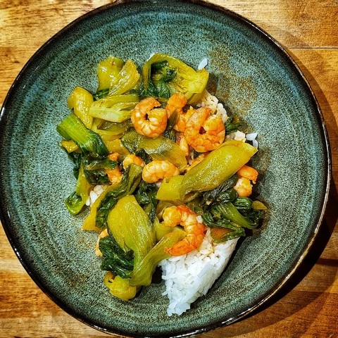 a greenish bowl with tiny quarters of bok choy / pak choy, small red prawns in a reddish sauce, and (more than) a little rice underneath