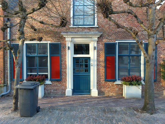Façade van een bakstenen huis met een deur met twee ramen aan weerszijden en een raam boven de deur op de eerste verdieping | Facade of a brick house with a door and two windows on both sides and another window above the door on the first storey.