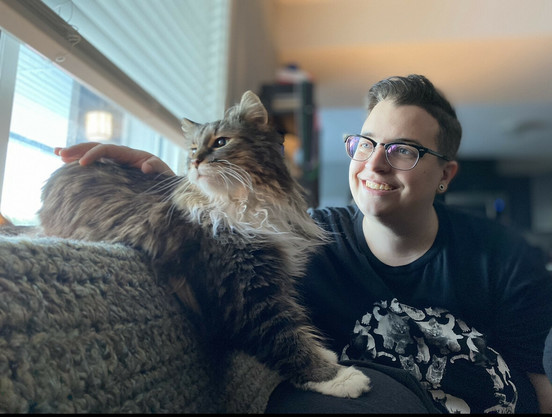 Me on the right in a black shirt and glasses looking out the window to the left with my cat, Patchy Mac, touching me with her paw, also looking to the left out the window.
