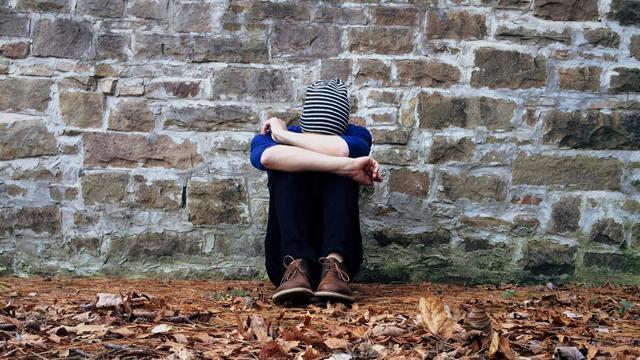 Person sitting against wall with head down.