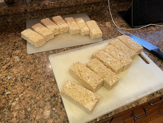 14 rectangular pieces of rice-and-marshmallow confections arranged on two plastic cutting boards.