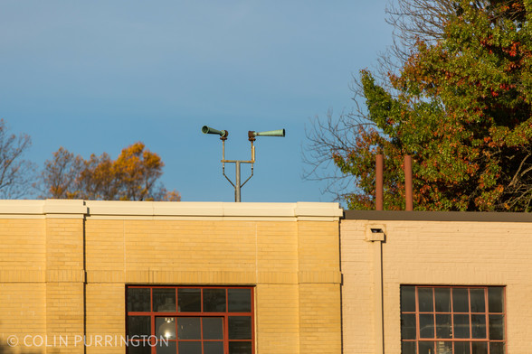 Two green metal horns on brackets atop a yellow brick building.