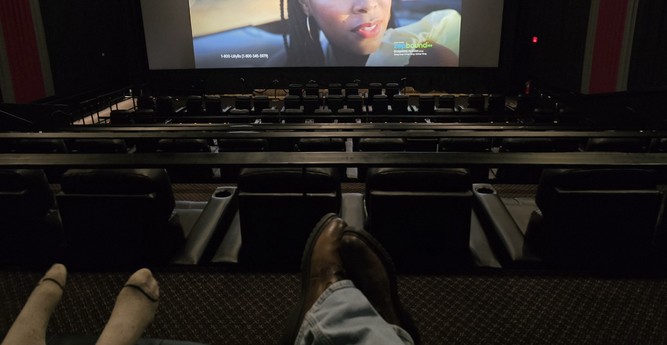 My daughter's and my feet with an empty theater below and a bit of the super screen.