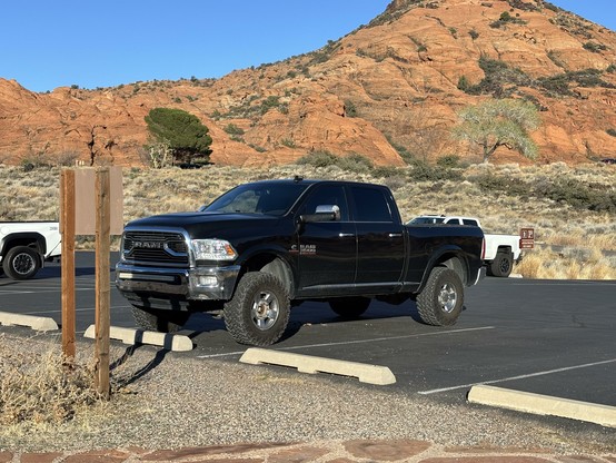 Black truck parked in a parking lot surrounded by red rock with blue sky.