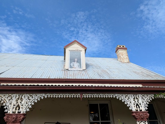 old federation style house roof with a gable window from which a mannequin looks out from