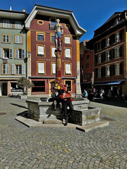 Two fursuiters posing infront of a historic fountain on a sunny day in the old city of Biel Bienne
