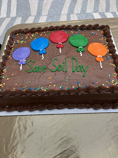 A big chocolate frosted sheet cake, decorated with icing balloons and the words Save Soil Day