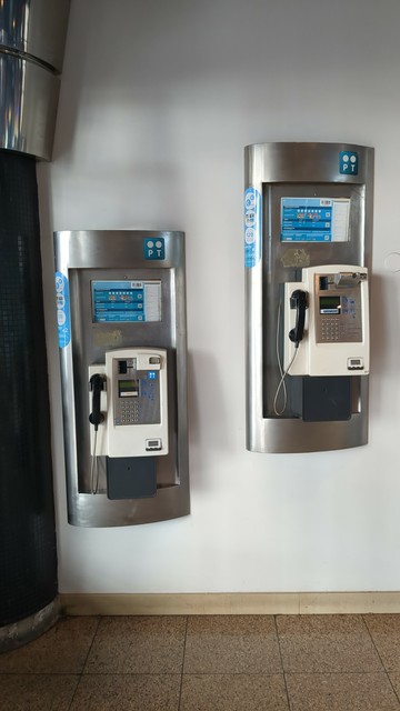 Dois telefones públicos numa parede branca. O telefone da esquerda encontra-se uns 30 centímetros mais baixo do que o da direita.