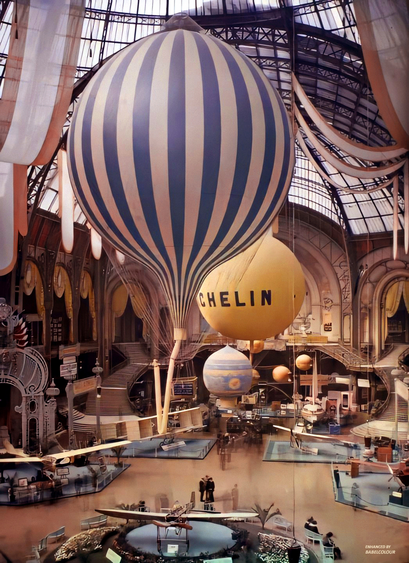 Photo of a large exhibition hall featuring ornate stone facades, glass vaults, grand staircases, and rich drapery. 

Several colourful hot air balloons are on display, including one with what appears to be the Michelin logo.

Stuart Humphryes, @official_babelcolour, cleaned & enhanced this autochrome taken at the first Paris Air Show, at the Grand Palais, by Léon Gimpel , on September 30th, 1909, less than 6 years after the Wright Brothers' first successful flight.