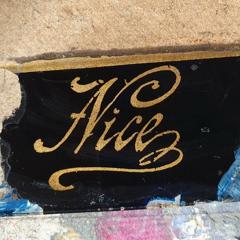 The word nice hand written in gold paint on a very dark blue background with flourishes circa 1929